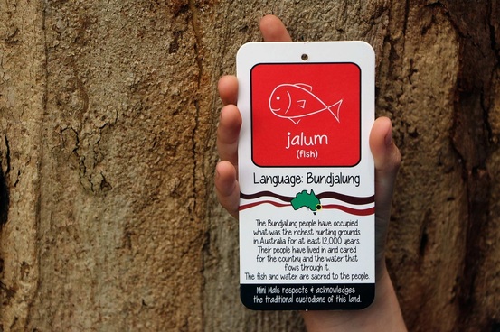 A child's hand holding up a Jalum T-Shirt tag which is a fish on a red background. 